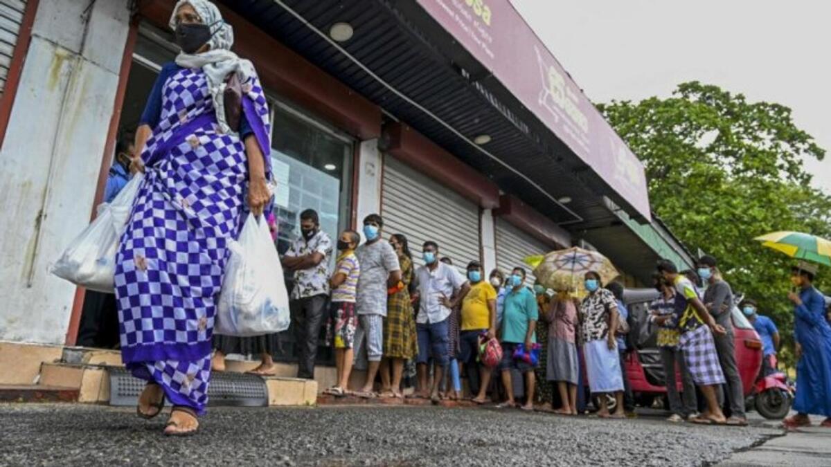 People stand in queue outside a state-run supermarket to buy essential food items in Colombo. – AFP