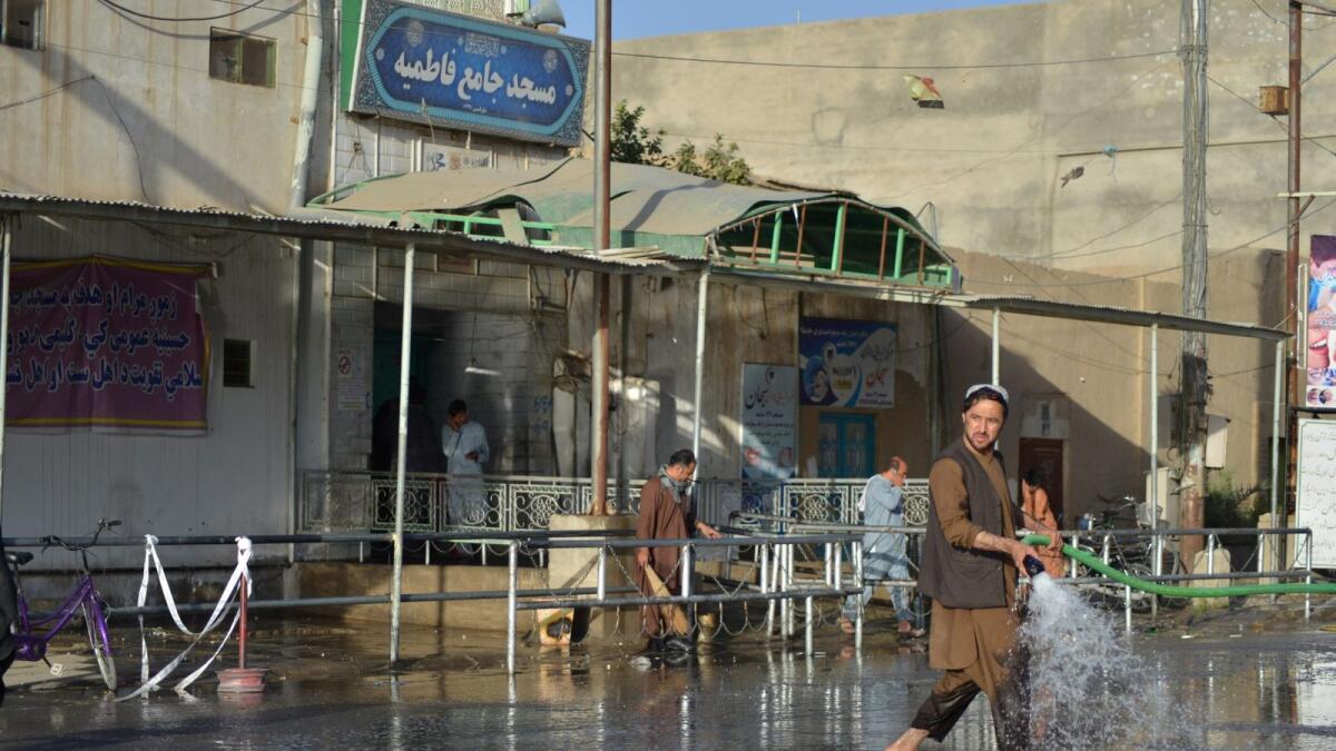 A man sprays water with a hose to clean a street outside a mosque in Kandahar after a bomb attack. – AFP