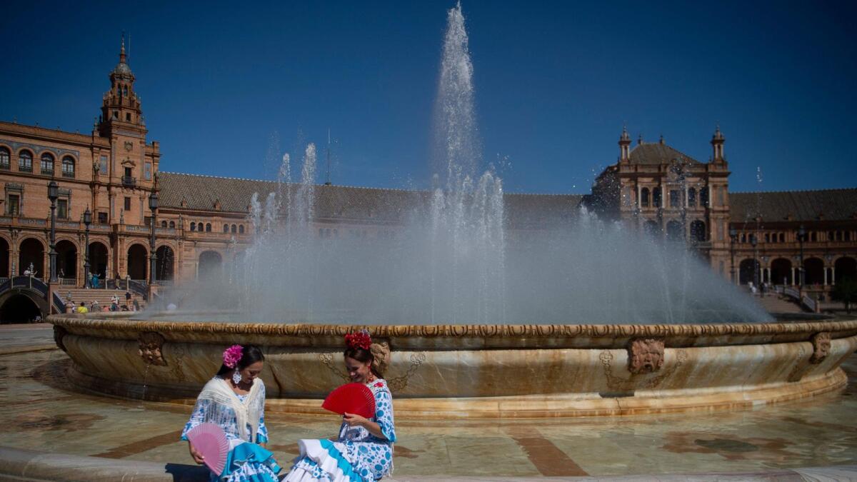 Women wearing traditional Andalusian dresses cool off with a fountain's water on Plaza de Espana in Seville as Spain is bracing for an early heat wave on  Monday. — AFP