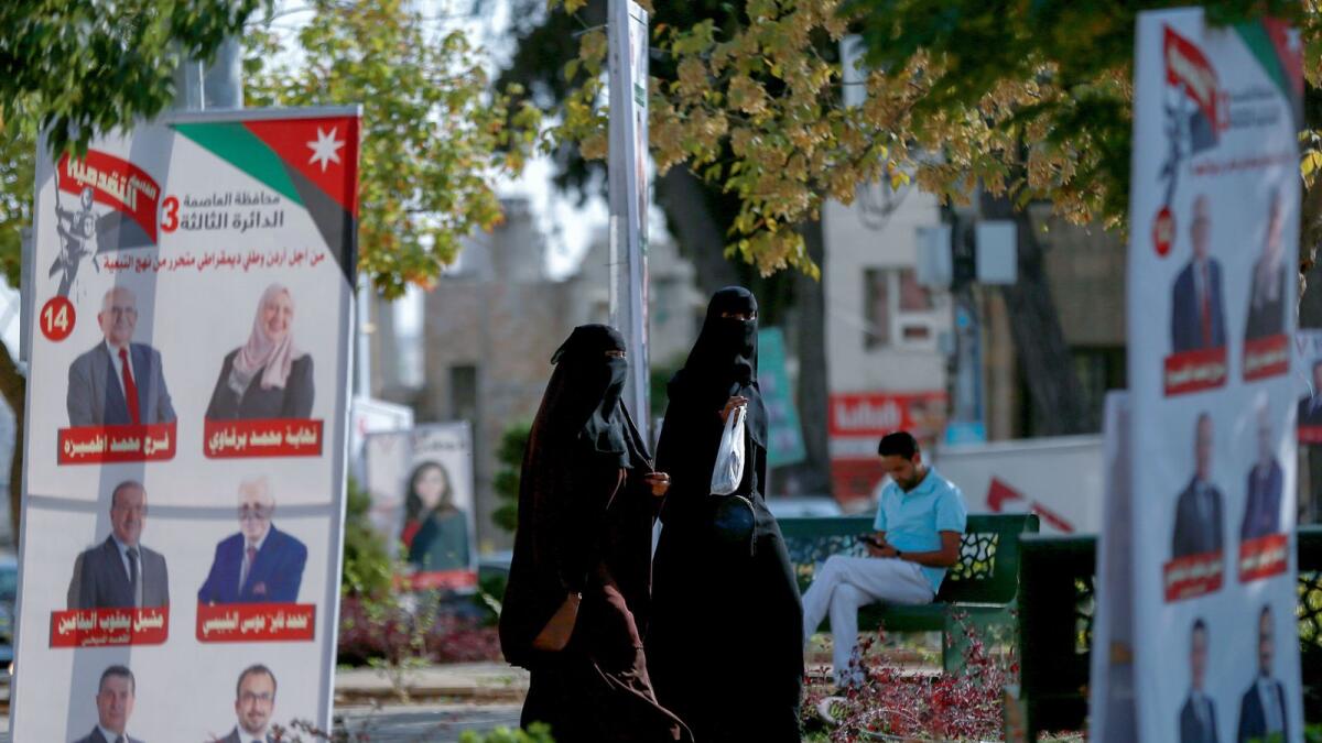Women walk in a park filled with campaign posters and slogans of candidates for the upcoming Jordanian parliamentary elections in Amman.