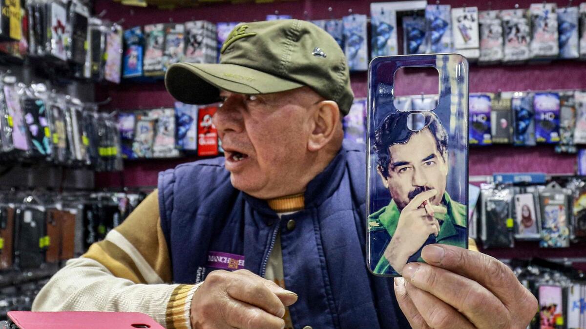 In this picture taken on April 5, 2023, Shaher Abu Sharkh, a 67-year-old Jordanian mobile phone accessory merchant holds up a cell phone cover showing the image of Iraq's late ousted dictator Saddam Hussein in his shop in Amman. — AFP