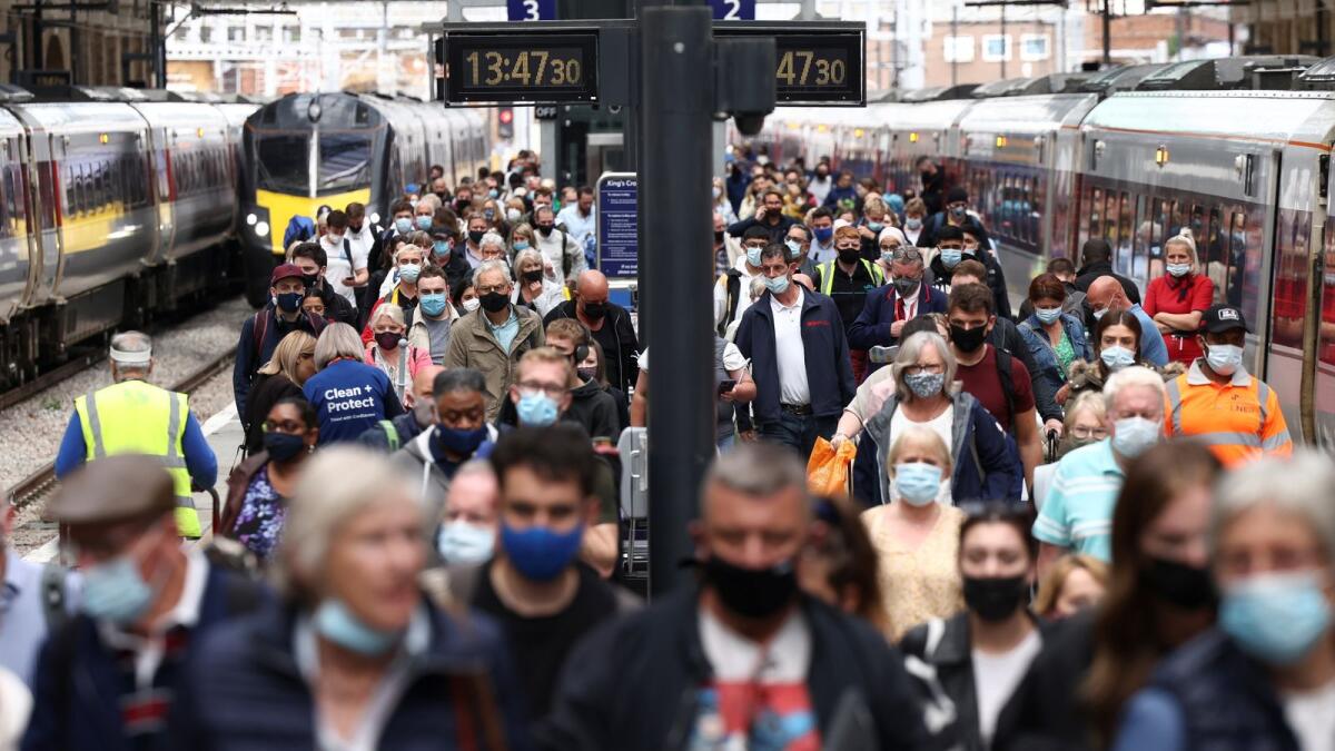 People wearing protective face masks walk along a platform at King's Cross Station in London.