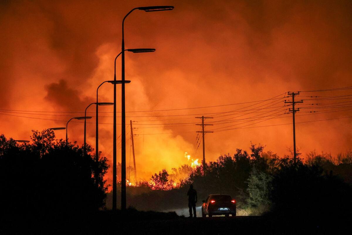 A man stands next to his car as a wildfire burns at the industrial zone of the city of Volos, in central Greece. — Reuters