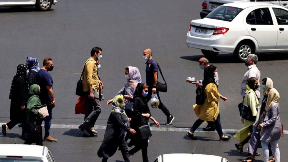 Mask-clad Iranians cross a street in the capital Tehran. — AFP