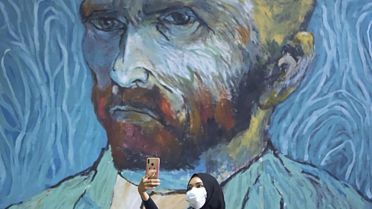 A visitor wearing a protective face mask takes a selfie near an art-wall painted by Indonesian artist Hanafi at Kertas Gallery during an exhibition in Depok, near Jakarta, Indonesia. Photo: Reuters