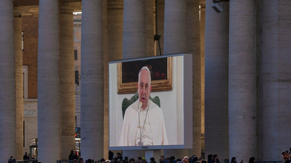 People watch Pope Francis on a giant monitor set up in St. Peter's Square at The Vatican on Sunday. - AP