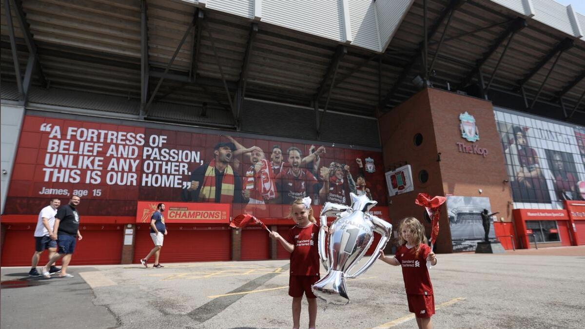 Children celebrate with a Premier League trophy balloon and flags outside Anfield after Liverpool were crowned Premier League champions. - Agencies