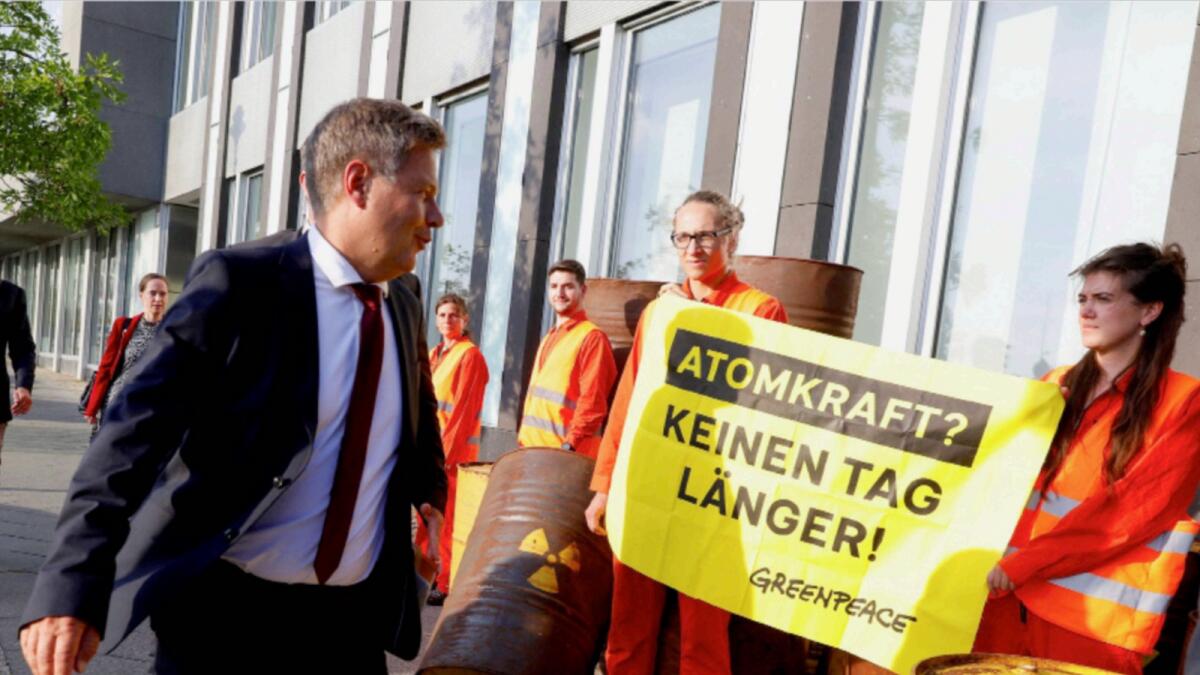 German Economy Minister Habeck walks past Greenpeace activists holding a banner that reads 'Nuclear power? Not one day longer!' as he arrives for a news conference. — Reuters