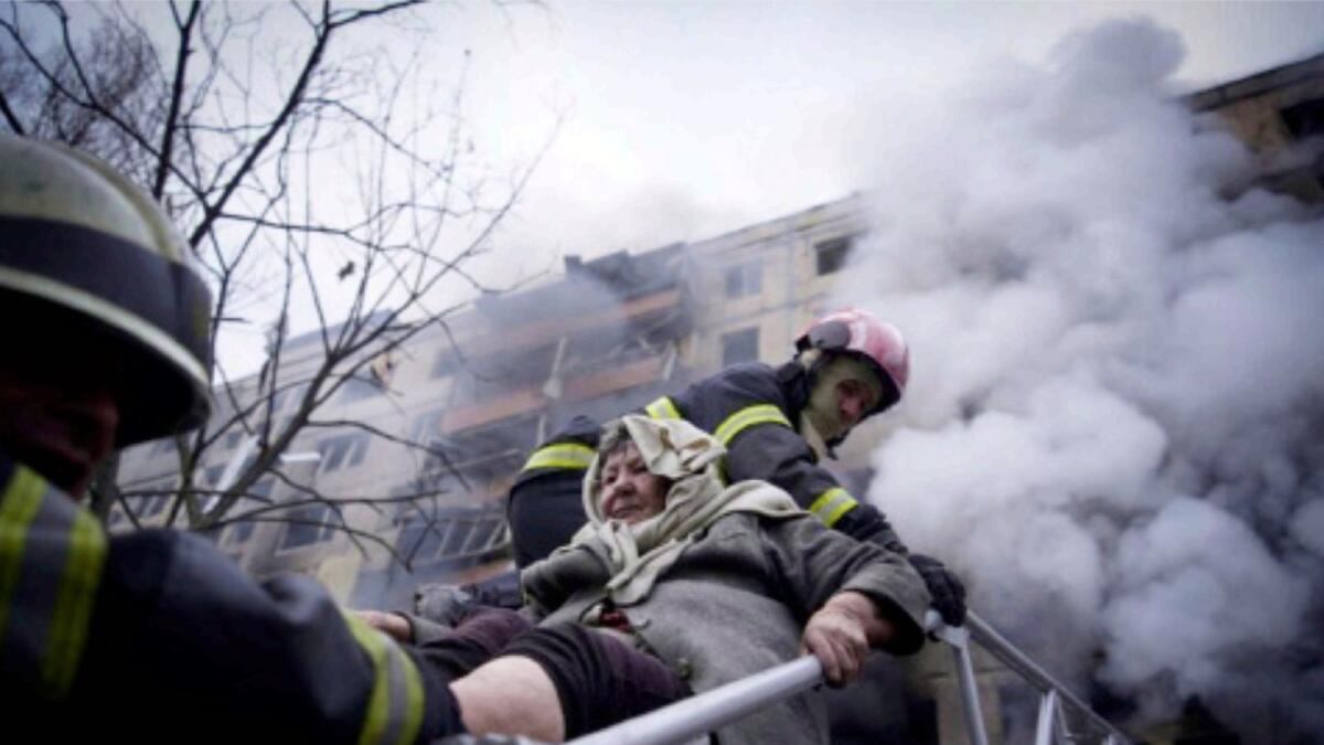 Firefighters evacuate an elderly woman from an apartment building hit by shelling in Kyiv. — AP