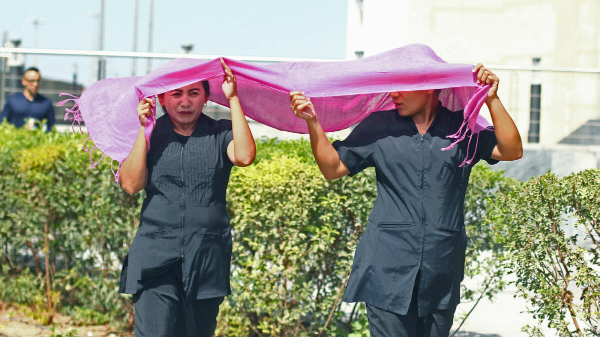 Two colleagues share a shawl to protect themselves from the sun in Downtown Dubai. -Photo by Shihab/Khaleej Times