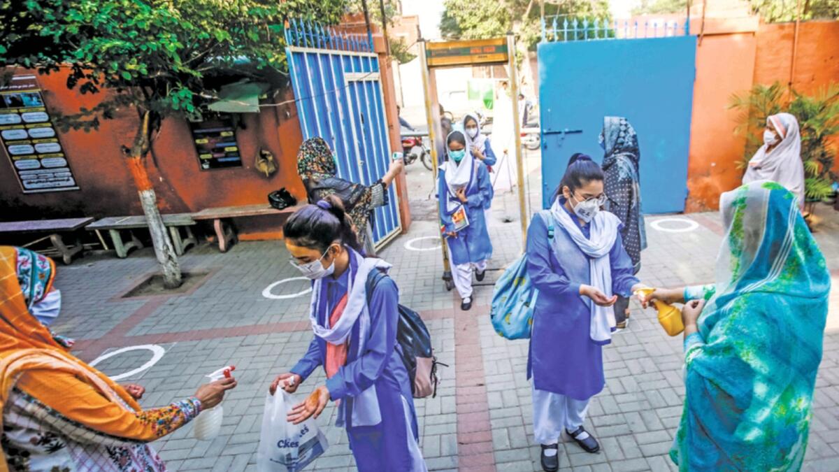 Teachers disinfect hands of students upon their arrival at a school in Lahore last September when the schools reopened. — AP file