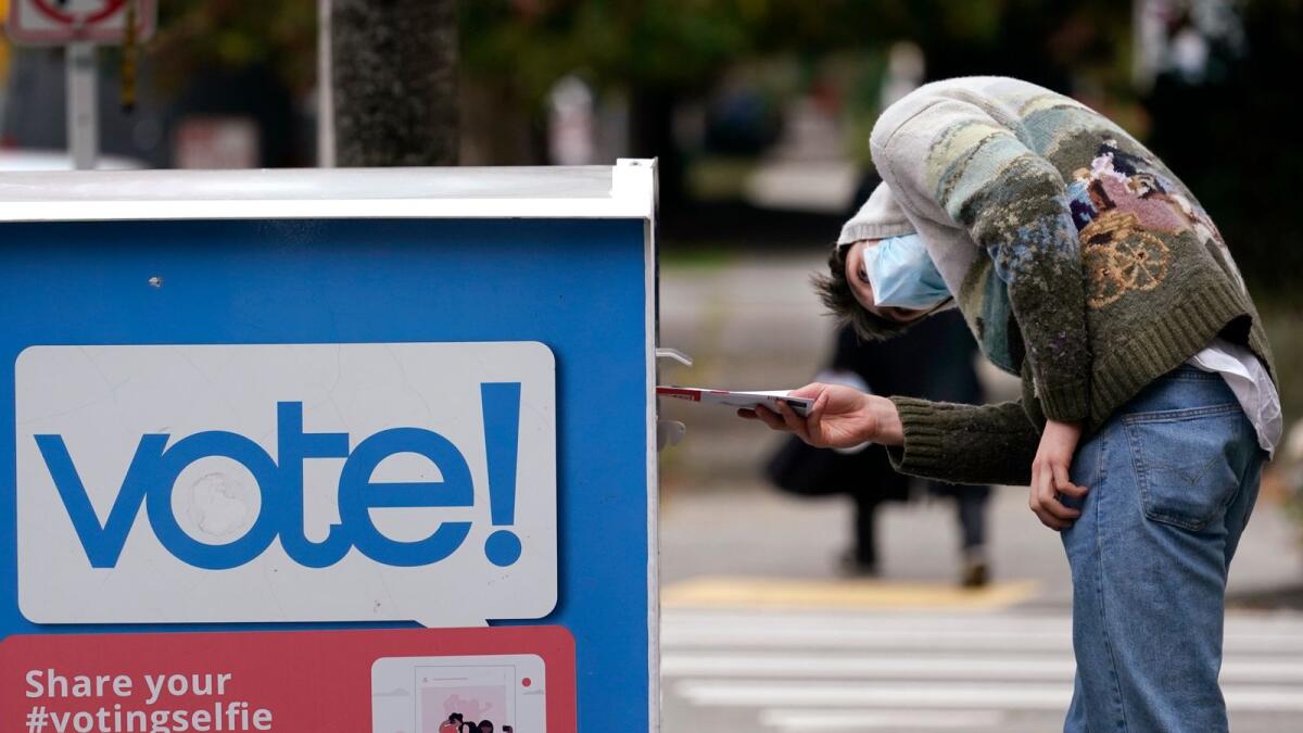 A voter turns sideways as he eyes the opening of a ballot drop box before placing his ballot inside it in Seattle.