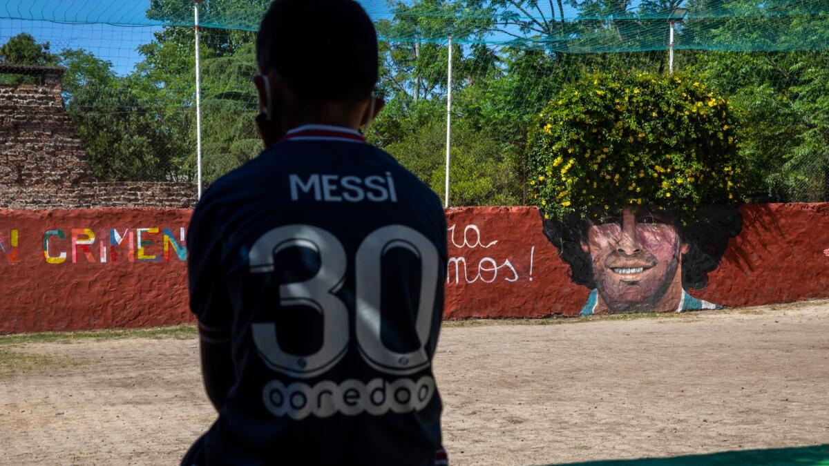A boy wearing a PSG Leonel Messi jersey rests near a mural of the late soccer star Diego Maradona at 'Lugar del Sol', a charity organization helping children at risk, in Buenos Aires, Argentina, Wednesday, Nov. 24, 2021. The first anniversary of the soccer legend's death is on Nov. 25. (AP Photo/Rodrigo Abd)