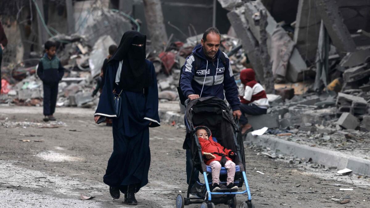 Members of a Palestinian family walk near a building destroyed by overnight Israeli bombardment in Rafah. — AFP