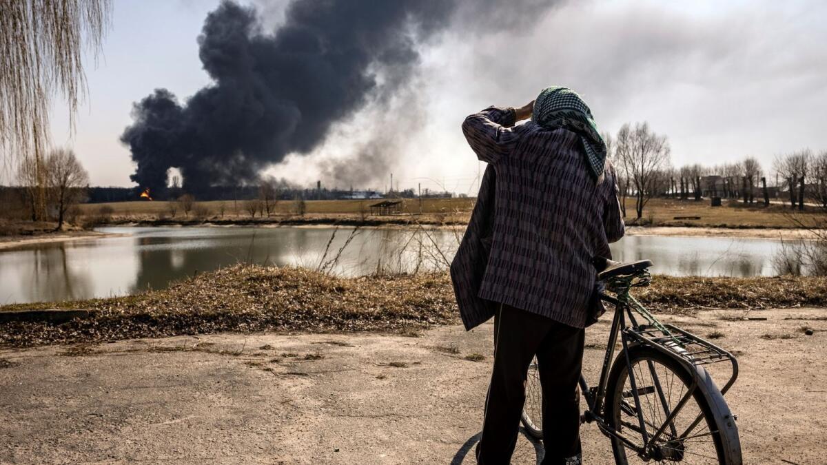 A man stands while smoke rises after Russian attacks hit a fuel storage facility in Kalynivka. – AFP