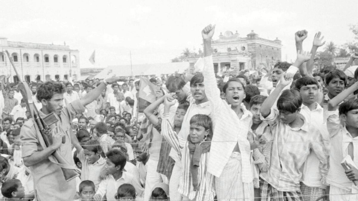 In this Dec. 11, 1971, file photo, a Mukti Bahini soldier, left, tries to keep the crowd under control as they cheer the acting Bangladesh president and the acting government during a public meeting in Jessore, East Pakistan. The city Hall with Indian soldiers standing guard on the roof is seen behind. Bangladesh is celebrating 50 years of independence this year. — AP file