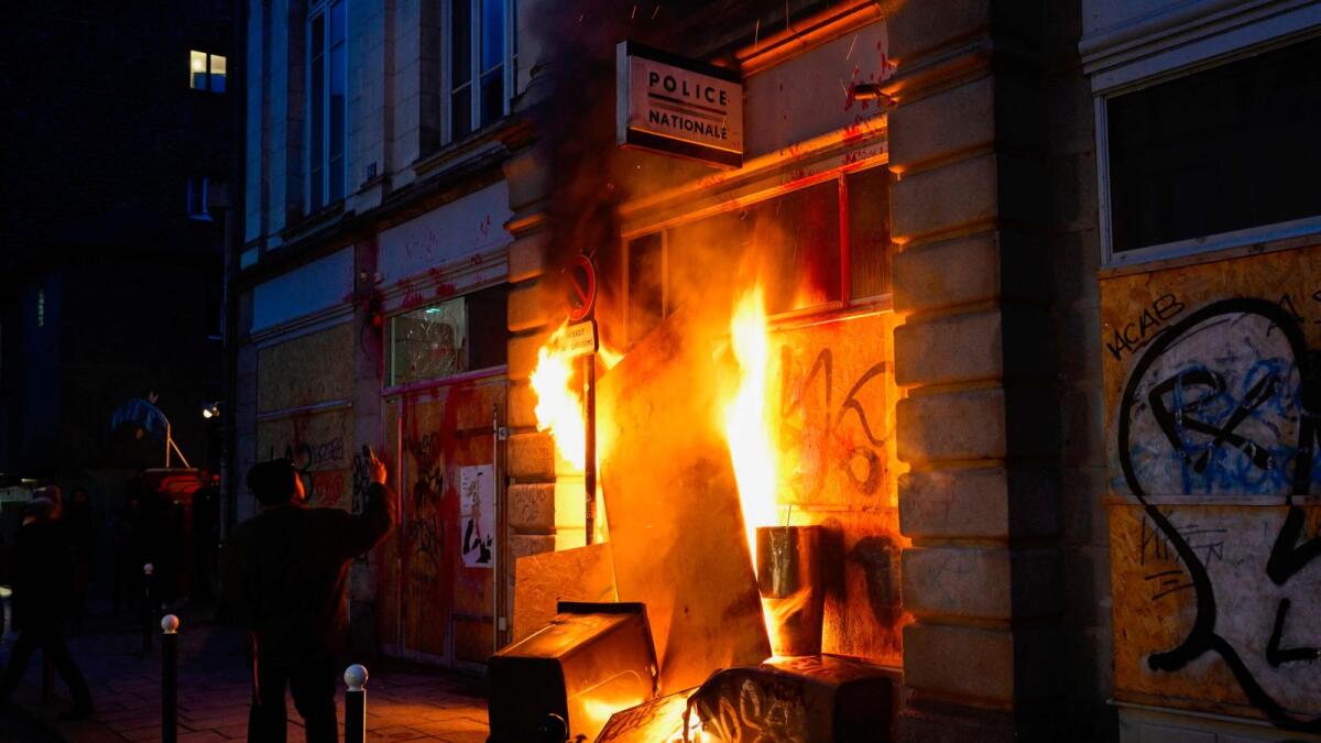 A pedestrian takes a picture of a police station on fire during a demonstration, after France's Constitutional Council approved the key elements of French President's pension reform, in Rennes, western France. — AFP