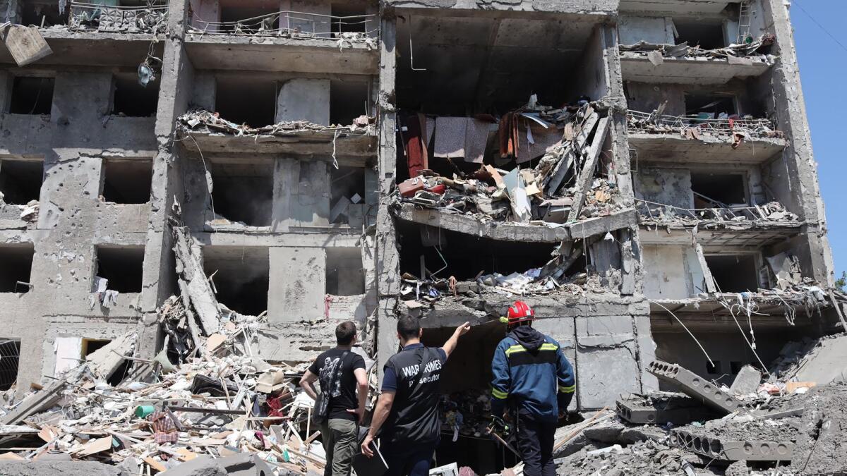 A war crimes prosecutor (C) and a rescuer (R) and a civil,  look at a destroyed building after being hit by a missile strike in the Ukrainian town of Sergiyvka , near Odessa, killing at least 18 people and injuring 30, on July 1, 2022. - During the night from June 30 to July 1, 2022, two missiles were fired by a 'strategic aircraft' from the Black Sea, hitting buildings, according to the Ukrainian emergency services. (Photo by Oleksandr GIMANOV / AFP)