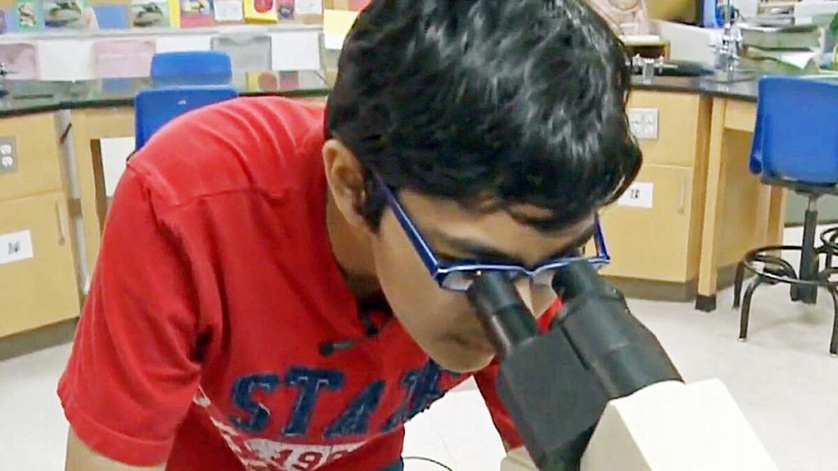 In this recent but undated frame from video provided by KOVR-TV, Tanishq Abraham, 12, looks into a microscope in a lab at American River College in Sacramento, Calif.