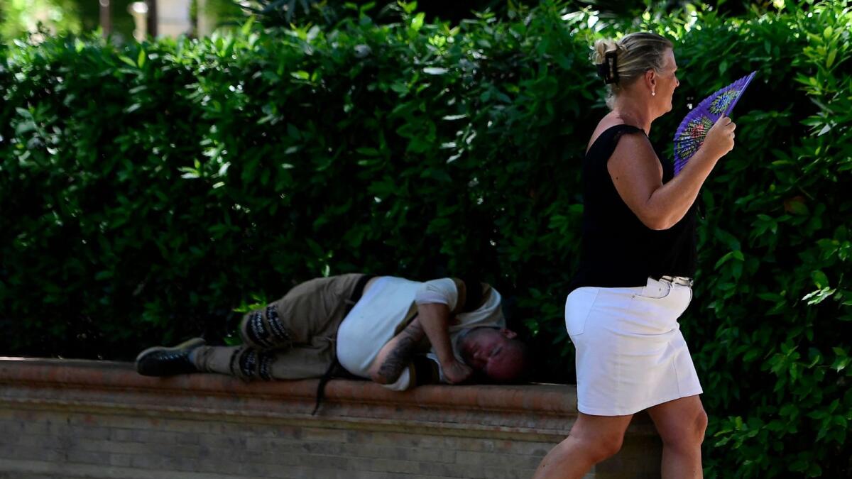 A woman using a fan to cool-off walks past a man lying in the shade in Seville on April 26, 2023 as Spain is bracing for an early heat wave. — AFP