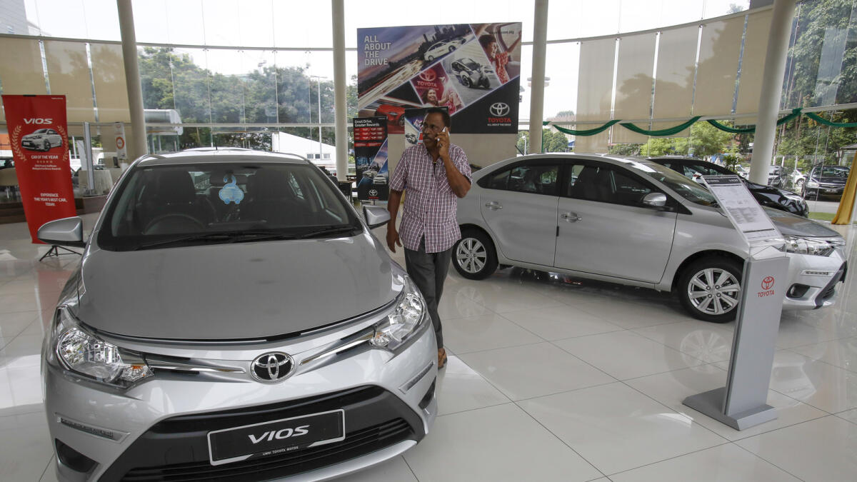 In this Tuesday, May 24, 2016 photo, a Malaysian man talks on his mobile phone while looking at a Toyota Vios on display at a sales showroom in Kuala Lumpur, Malaysia.  Japanese automaker Toyota Motor Corp. said it will build a second factory in Malaysia as part of expansion to meet rising local demand. (AP Photo/Joshua Paul)