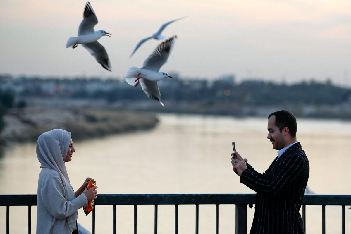 Seagulls fly as man snaps a picture of a woman over the Jadriya Bridge on the Tigris River in Baghdad, Iraq, on January 17, 2024.  — AFP file