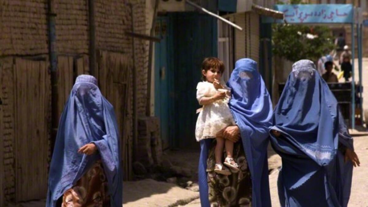 Three Afghan women walk a deserted street .