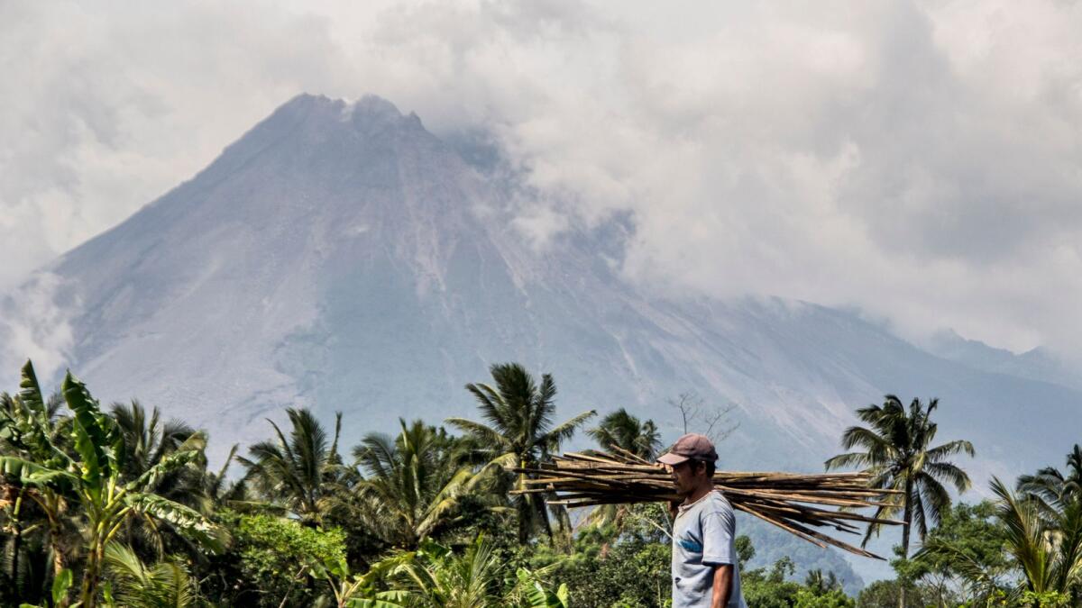 A farmer walks on his field as Mount Merapi is seen in the background in Sleman, Indonesia, on Thursday.