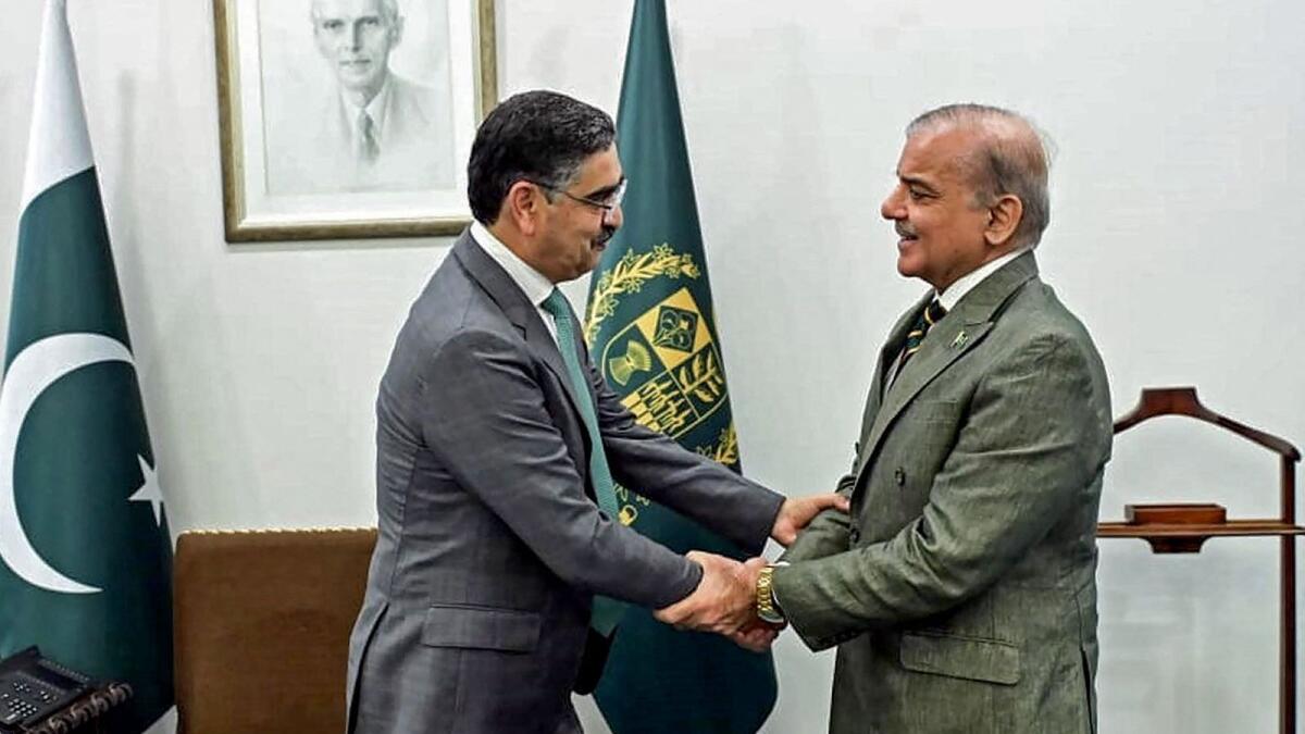 Pakistan's newly appointed caretaker Prime Minister, Anwaar-ul-Haq Kakar (L) and outgoing Prime Minister Shehbaz Sharif shake hands at the President House in Islamabad. - AFP