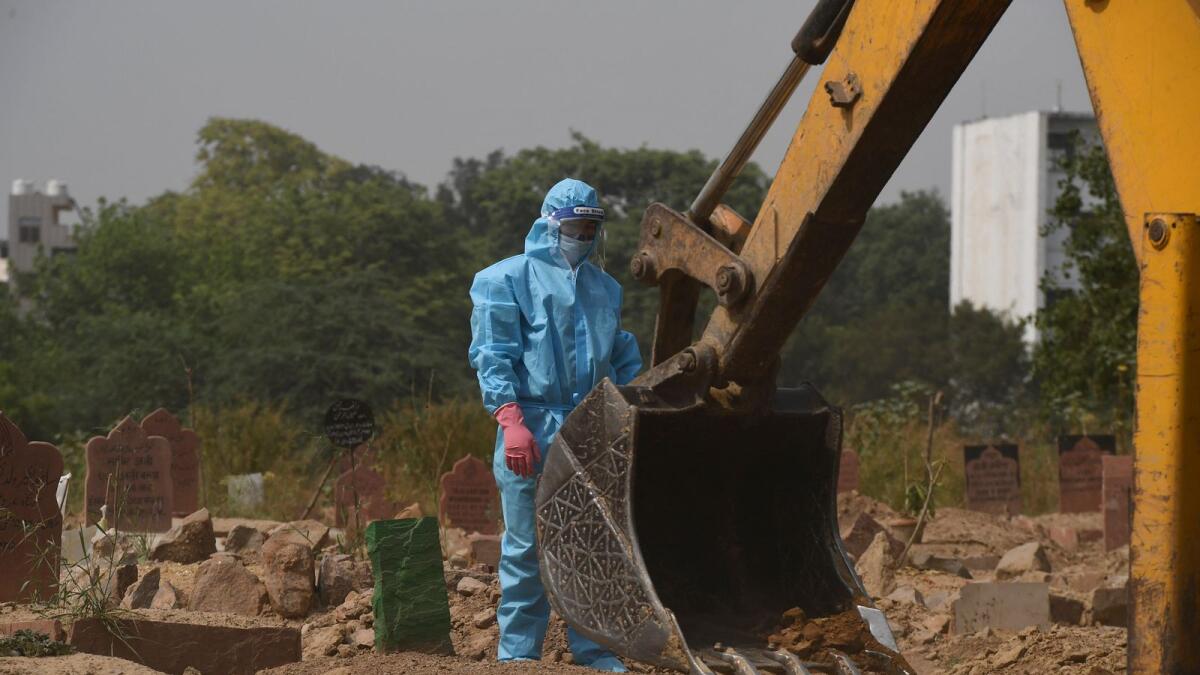 A relative wearing a personal protective equipment suit looks on as an excavator covers the grave of his loved one, who died from Covid. Photo: AFP