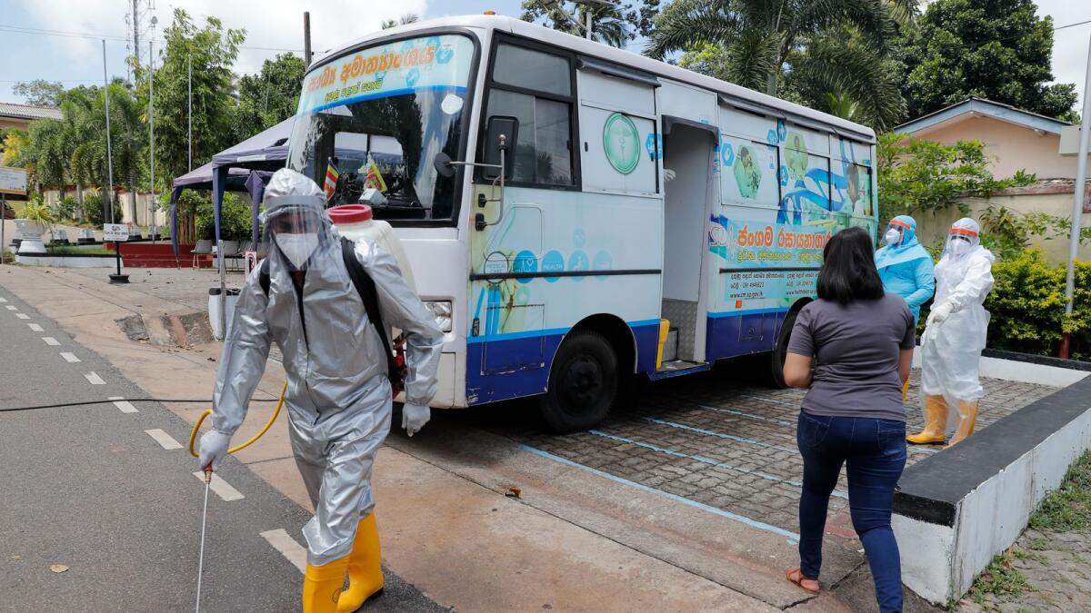A Sri Lankan health worker sprays disinfectants as people wait to give swab samples to test for Covid-19 near a mobile testing vehicle outside a hospital. AP Photo