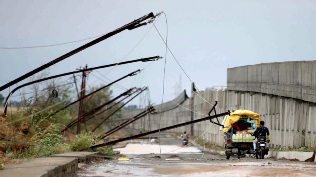People move past electricity poles damaged by cyclone Tauktae in Gujarat. — Reuters