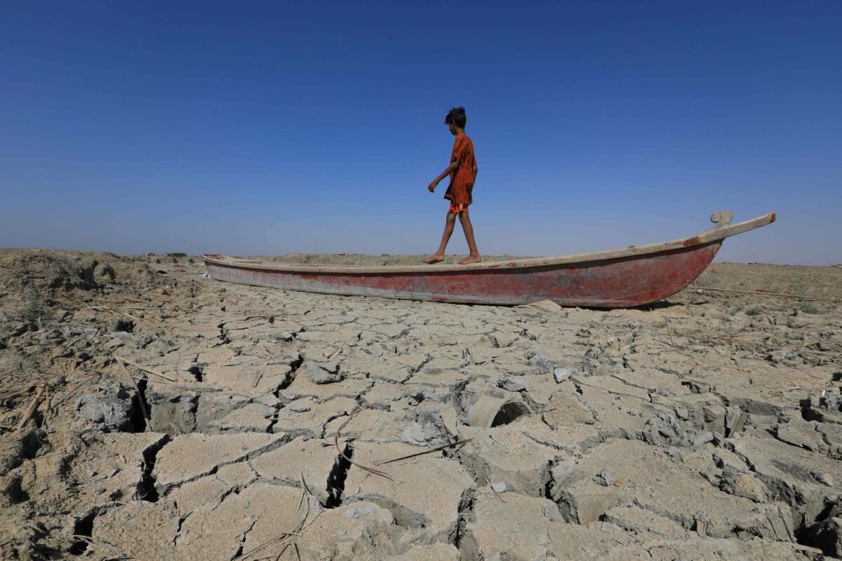 A boy walks on a boat left lying on the dried-up bed of a section of Iraq's receding southern marshes of Chibayish in Dhi Qar province on June 28, 2022. — AFP