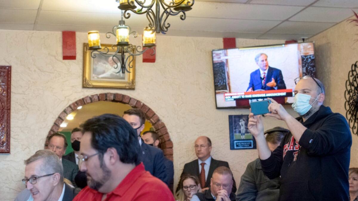 Texas Governor Greg Abbott delivers announcement on doing away with Covid restrictions, broadcast on the TV in the background, as a crowd watches him make it at Montelongo's Mexican Restaurant on Tuesday. — AP