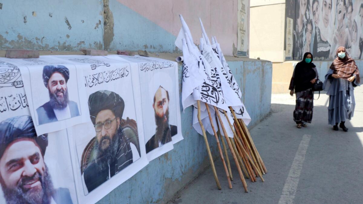 Afghan women walk by posters of Taliban leaders and flags in Kabul. — AP