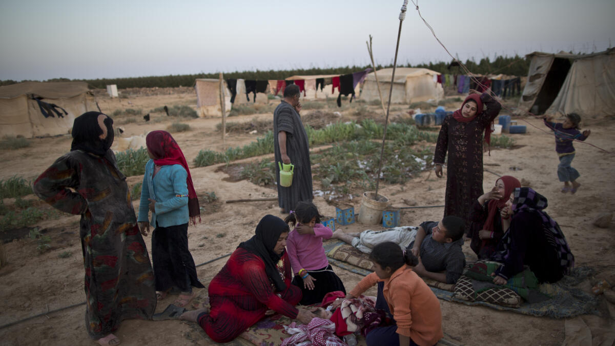 A woman sits next to her sick infant and other refugees outside their tent.