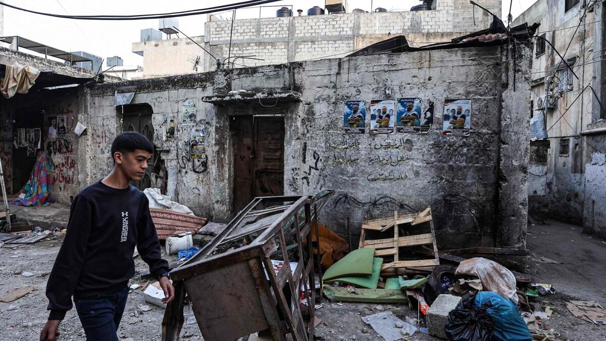 Palestinians walk past damage on a street in the aftermath of an Israeli raid at the Balata refugee camp. — AFP