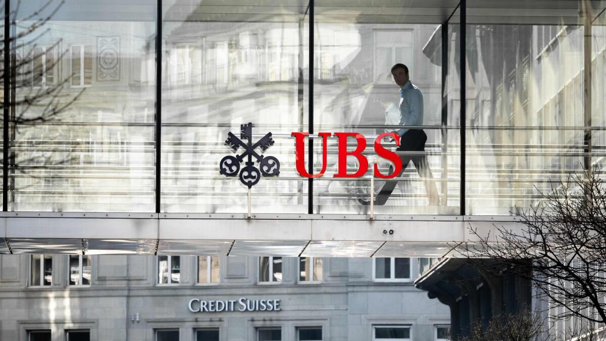 A employee is seen in silhouette next to a sign of Swiss giant banking UBS and a sign of Credit Suisse bank in Zurich on Monday. UBS share price plunged on March 20, 2023 as a deal to take over its troubled Swiss rival Credit Suisse for $3.25 billion failed to calm stock market nerves. - AFP