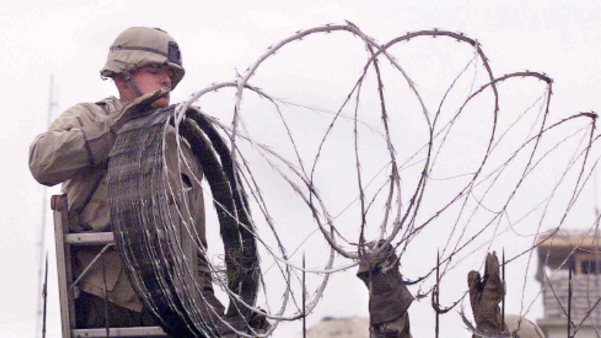 US Marine is given a hand using barbed wire to secure the walls the US embassy in Kabul on January 11, 2002. — AFP file