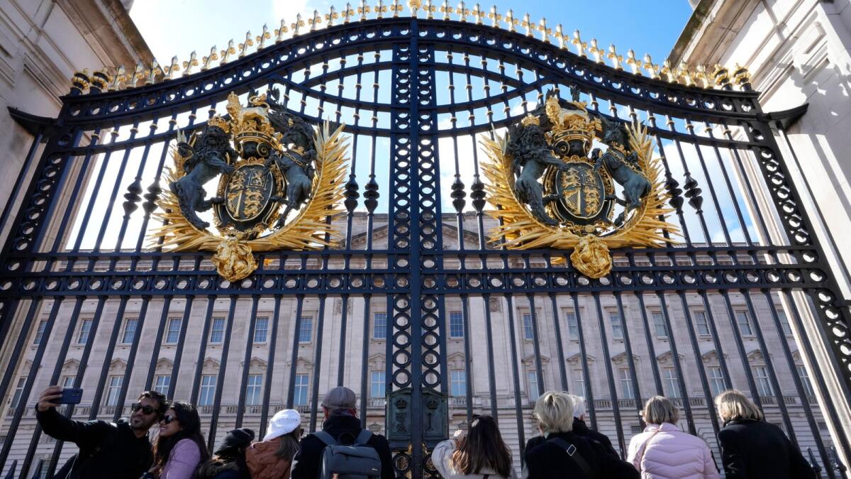Tourists pose for a photograph in front of the main gates to Buckingham Palace in London on Sunday. — AP