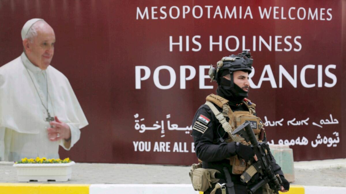 A security man walks near a poster of Pope Francis upon his visit to Iraq in Baghdad. — Reuters