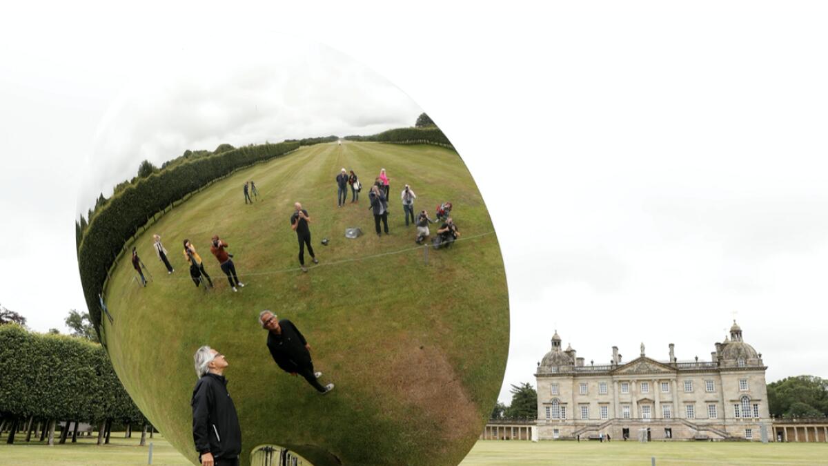 British-Indian artist Anish Kapoor is reflected in one of his sculptures as he poses for photographs in the gardens at Houghton Hall in Norfolk, Britain. Photo: Reuters