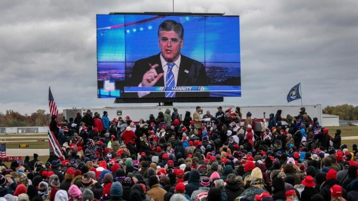 A large screen shows Fox News anchor Sean Hannity at a Trump rally in Waterford, Michigan.