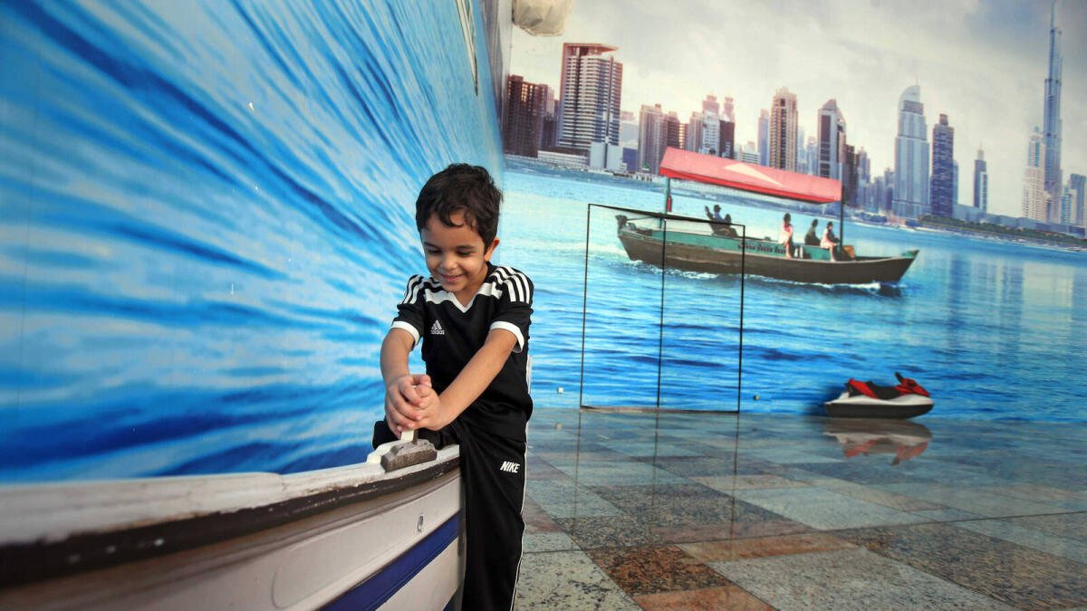 A kid plays with a boat decor showing backdrop of the Dubai Creek at the Dubai Festival City.- Photo by Dhes Handumon/ Khaleej Times