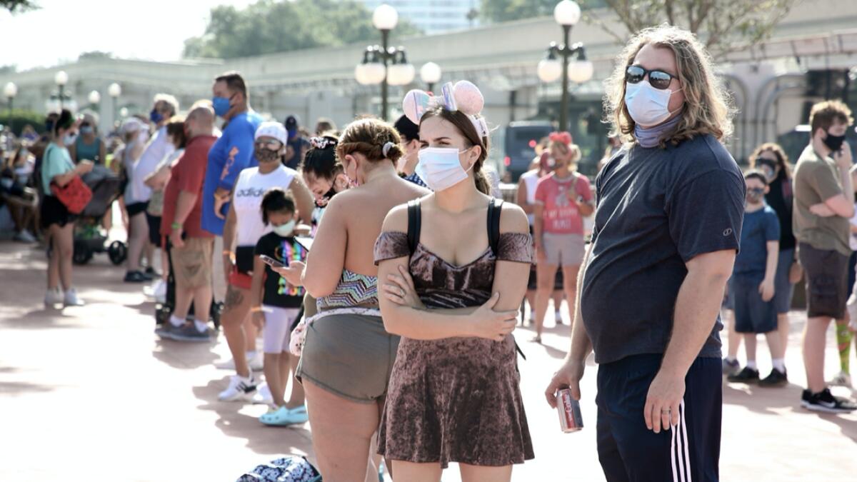 Guests wearing protective masks wait outside the Magic Kingdom theme park at Walt Disney World on the first day of reopening, in Orlando, Florida, on July 11, 2020.  In the distance at right is the newly repainted Cinderella Castle. Disney's flagship theme park reopened its doors to the general public on Saturday, along with Animal Kingdom, as part of their phased reopening in the wake of the Covid-19 pandemic. New safety measures have been implemented including mandatory face masks for everyone and temperature checks for guests before they enter. Photo:  AFP