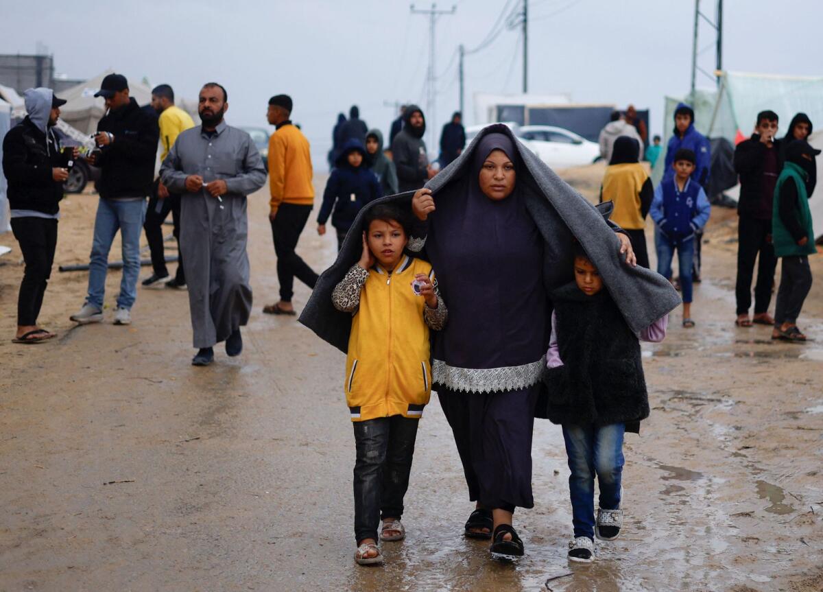 Displaced Palestinians, who fled their houses due to Israeli strikes, walk following heavy rains at tent camps.