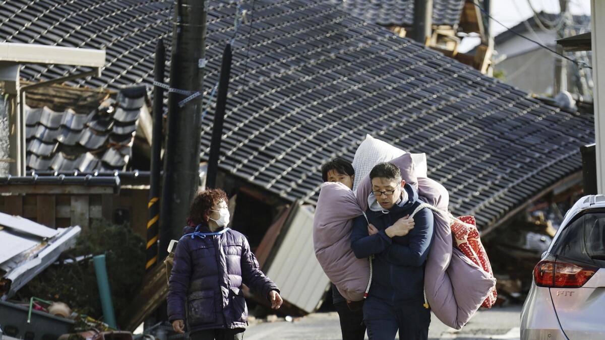 People carry bedclothes through fallen houses hit by earthquakes and tsunami in Suzu. — AP
