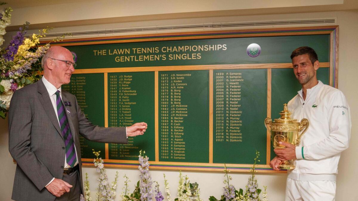 Serbia's Novak Djokovic holds the winner's trophy as he stands with Ian Hewitt, AELTC Chairman, in front of the honours board. — AFP