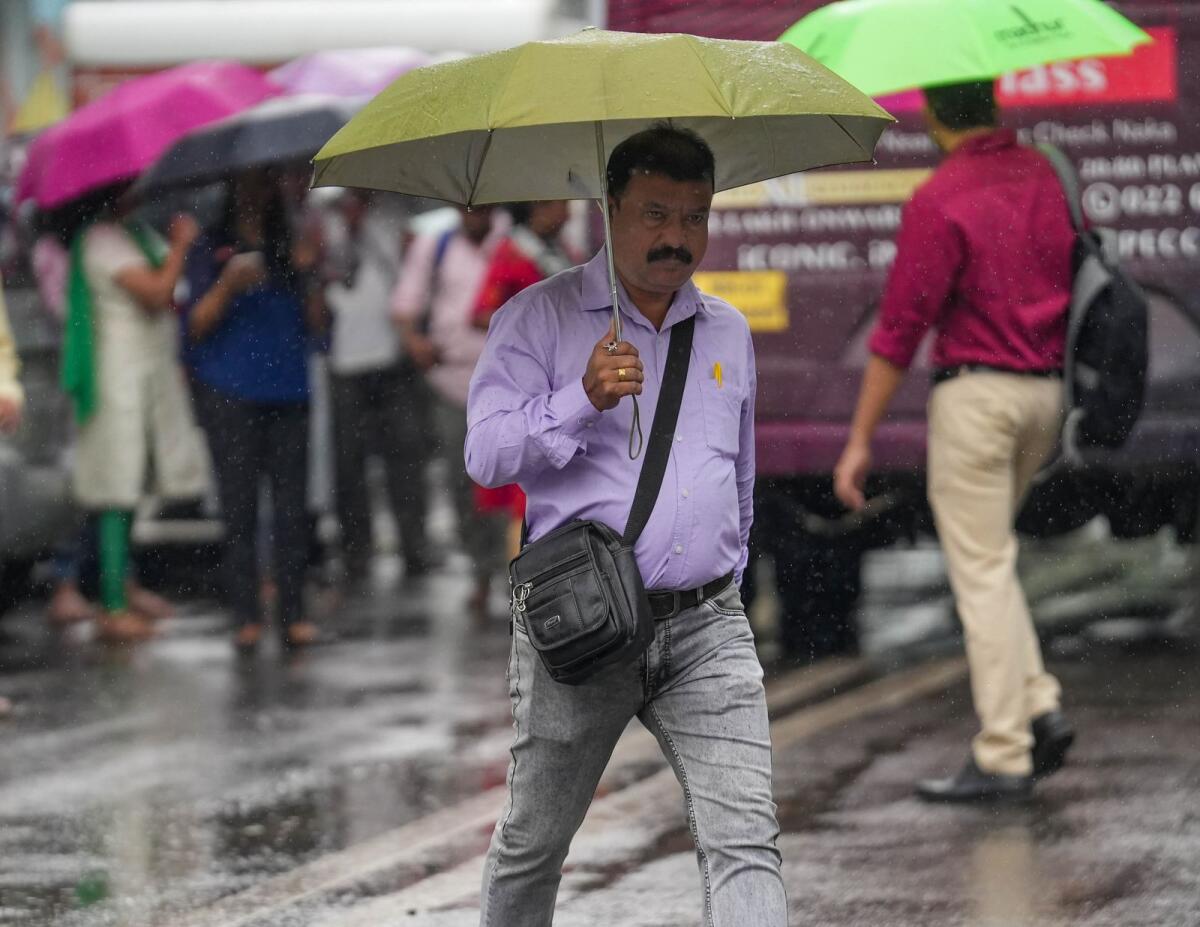 A pedestrian holds an umbrella to protect himself from rain as he crosses a road in Mumbai on March 21, 2023. Photo: PTI