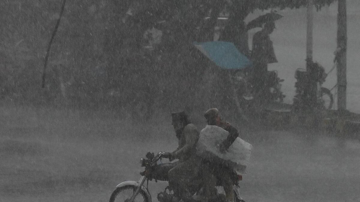 Motorcyclists ride a motorbike along a street during a rainfall in Lahore. — AFP